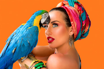 Portrait of young attractive woman in african style with ara parrot on her hand on colorful background