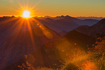 red orange sunset with sunbeams to grass in tyrol mountains