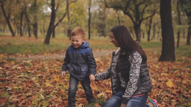 Cheerful red-haired little boy with his mother compre throw up yellow leaves in autumn park