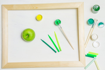 Green apple and paintbrushes in a wooden frame
