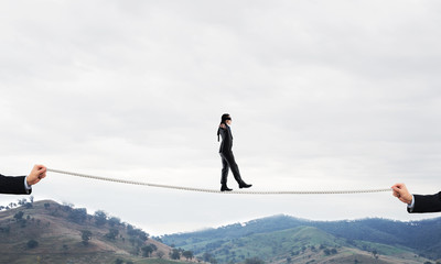 Business concept of risk support and assistance with man balancing on rope
