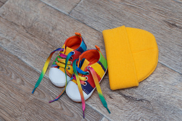 children's colored shoes and a yellow hat on wood background 