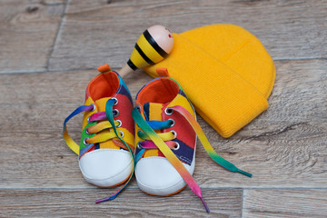 children's colored shoes and a yellow hat on wood background 