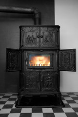 Colorkey-Foto eines schönen historischen Gussofens in einem alten Haus mit schön warmen Feuer hinter glänzender Kaminscheibe