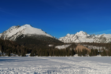 Fototapeta na wymiar Winter view of frozen surface of Strbske Pleso (Tarn) with hotel and peaks of High Tatra mountains in background. Strbske Pleso is second largest glacial lake on the Slovak side of High Tatras.