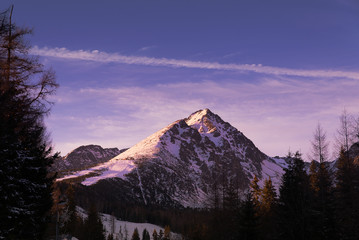 View of scenic fairy-tale snowy mountain peak. Winter wonderland mountain  in the High Tatra mountains with snow and dramatic clouds in the sky in beautiful evening light during blue hour at dusk - 133249055