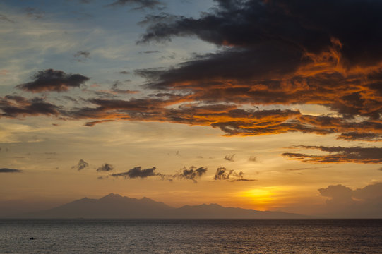 Sunrise Over Lombok Island, Indonesia. A dramatic sunrise over the Lombok Strait to the island of Lombok as seen from the Amed area of eastern Bali, Indonesia. Balinese fishing boats on the horizon.