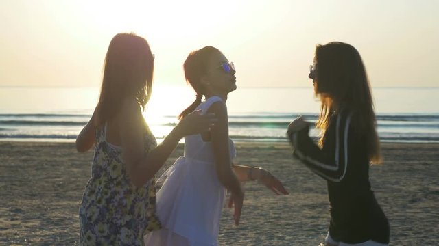 Three beautiful young women dancing on the beach at sunrise