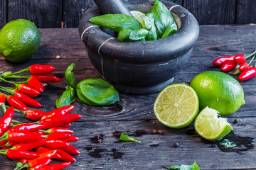 Fresh basil in dark mortar and fresh chilly and lime