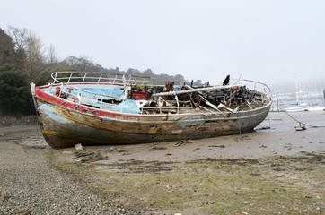 Fototapeta na wymiar Burnt out ship wreck, boat fire damage, beached on coast shore line, fishing motor boat