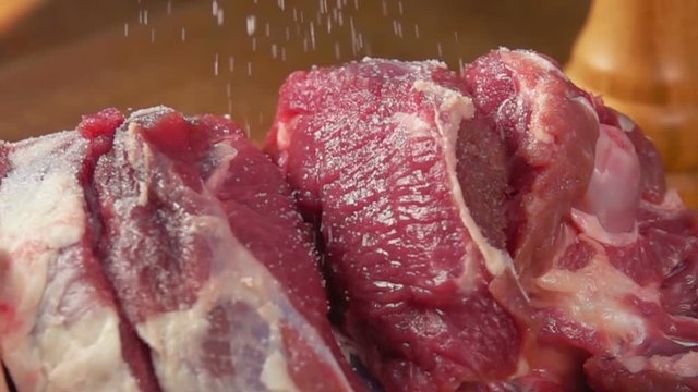 Close-up of salt falls on the leg of lamb in slow motion