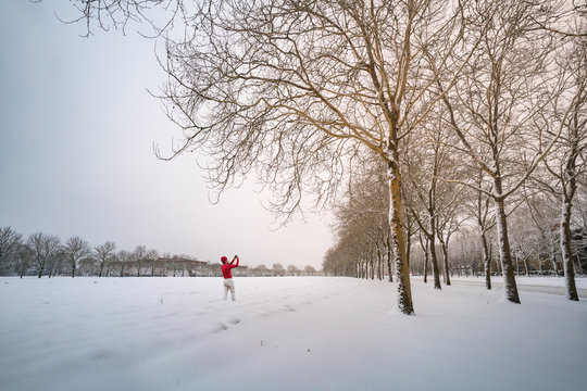 Man in red taking picture of snowy field and trees