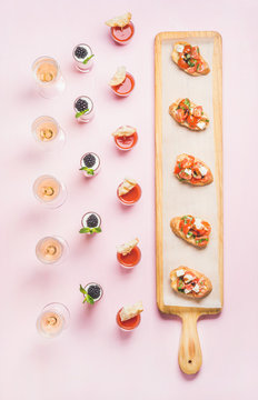 Catering, banquet food concept. Various snacks, brushetta sandwiches, gazpacho shots, desserts with berries on corporate event, christmas, birthday, wedding celebration over pink background, top view