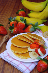 Delicious pancake with sliced of strawberry and banana on white plate and fresh fruit on wooden table.
