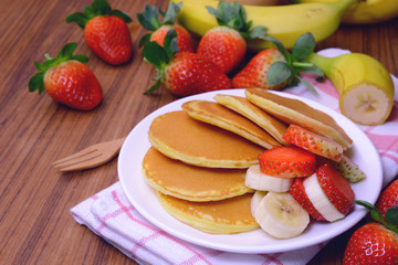 Delicious pancake with sliced of strawberry and banana on white plate and fresh fruit on wooden table.