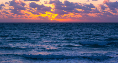 Obraz premium Sunset over the ocean with violet clouds. Scenic sunset over the ocean.