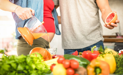 Young couple with pregnant woman at cooking in kitchen with healthy vegetarian food - Love food concept with people at home preparing vegan lunch with bio vegetables - Focus on pressed juice squeezer