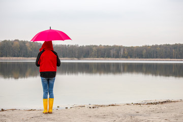 eine Frau steht bei kaltem, nassen Wetter mit einem Regenschirm an einem See