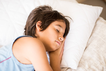 Kid in bedroom sleepin on bed with white sheet and pillow