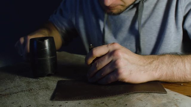 Man working on leather, making holes using hummer