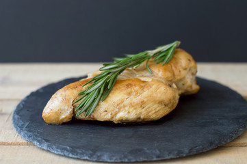 Fried chicken breast with fresh rosemary on small slate board on wooden table, black background