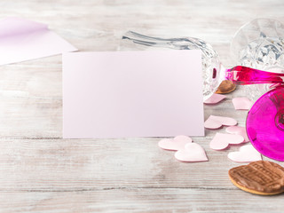 Empty pink paper note with two stemmed champagne glasses pink hearts and chocolate cookies on wooden textured background. Valentine's day wedding romantic date invitation