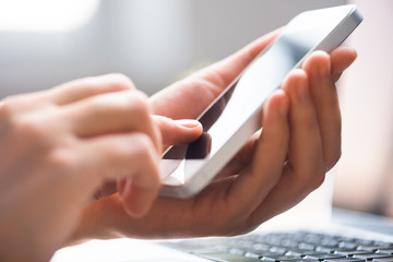 Finger pointing to phone screen, laptop in the background, informal business atmosphere