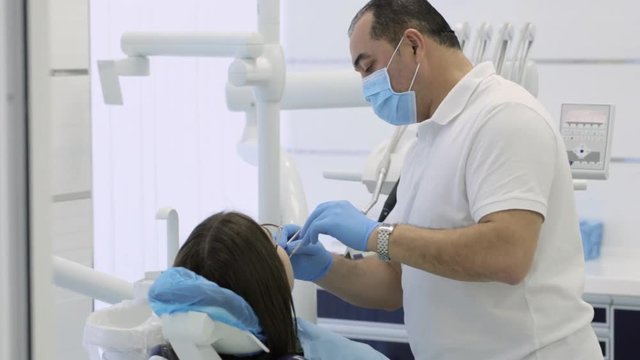 Male dentist making procedure on young female patient at modern clinic