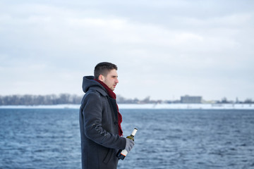 Fototapeta na wymiar Man drinking wine from a bottle on the shore of the river in the winter. Winter dipressiya.