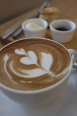 Coffee with Leaf Art with Scone in the Background