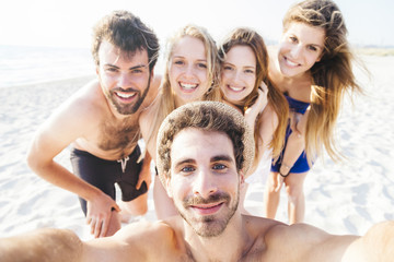 Selfie on the beach, summer day at sunset. Five friends in swimwear, two men and three women take photo near sea