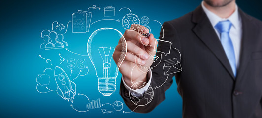 Businessman drawing a lightbulb with a pen with multimedia icons
