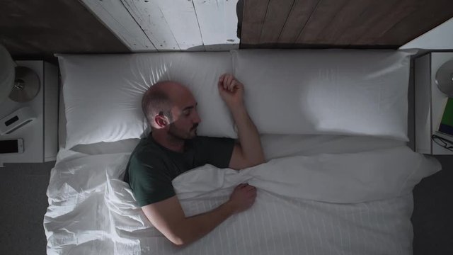 Young man sleeping deeply in her bed at night. High angle view.