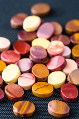 Colorful and polished mookaite jasper beads in oval shape on black weave.