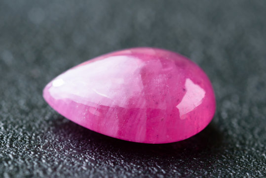 Pinkish red pear or drop shaped ruby cabochon on black cast iron plate.