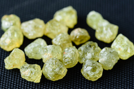 Collection of green uncut mali garnet gemstones on black weave.