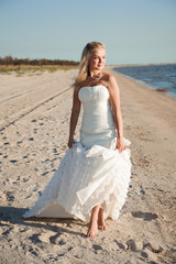 Fototapeta na wymiar Bride walking along sea coast wearing beautiful wedding dress