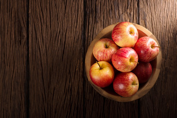 Red apples in a wooden bowl on dark background.