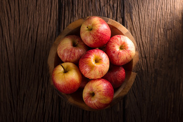 Red apples in a wooden bowl on dark background.
