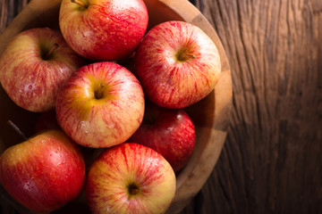 Red apples in a wooden bowl on dark background.