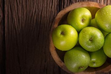 Green apples in wooden bowl on wooden table.