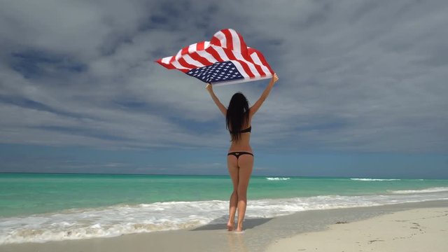 Young Woman In Bikini Stand A Back On The Beach With Usa Flag At Her Arms