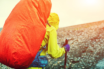 woman hiker on the trail in mountains, walking in the rain with a backpack in a raincoat and wearing a waterproof jacket.