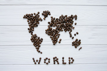 Map of the world made of roasted coffee beans laying on white wooden textured background with signature and space for text