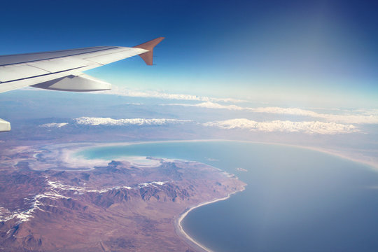 Image of plane and wing with sea, mountains, and coastline. Horizont line and sunrise.