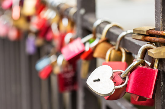 heart-shaped padlock hanging on rails among other variegated padlocks