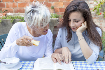 pretty mom and daughter reading a book while having breakfast ou