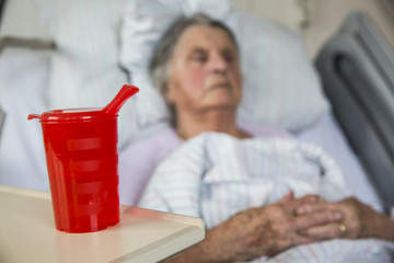 Seniorin im Krankenhaus trinkt aus einer Schnabeltasse