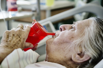 Seniorin im Krankenhaus trinkt aus einer Schnabeltasse
