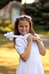 Śliczna dziewczynka w białej sukience trzyma świecę na ramieniu.